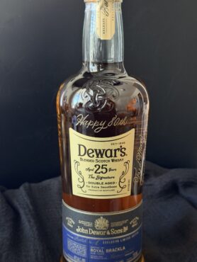 A bottle of Dewar's 25 Year Old Scotch whisky with "Happy 80th" hand engraved in flowing script on the glass just above the front label, shown against a dark background.