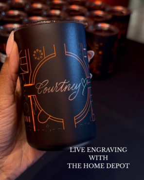 Hand holding a black matte tumbler with an orange geometric design, hand engraved with the name "Courtney" and a small heart in calligraphy script at a live engraving activation for The Home Depot by Captivating Calligraphy.